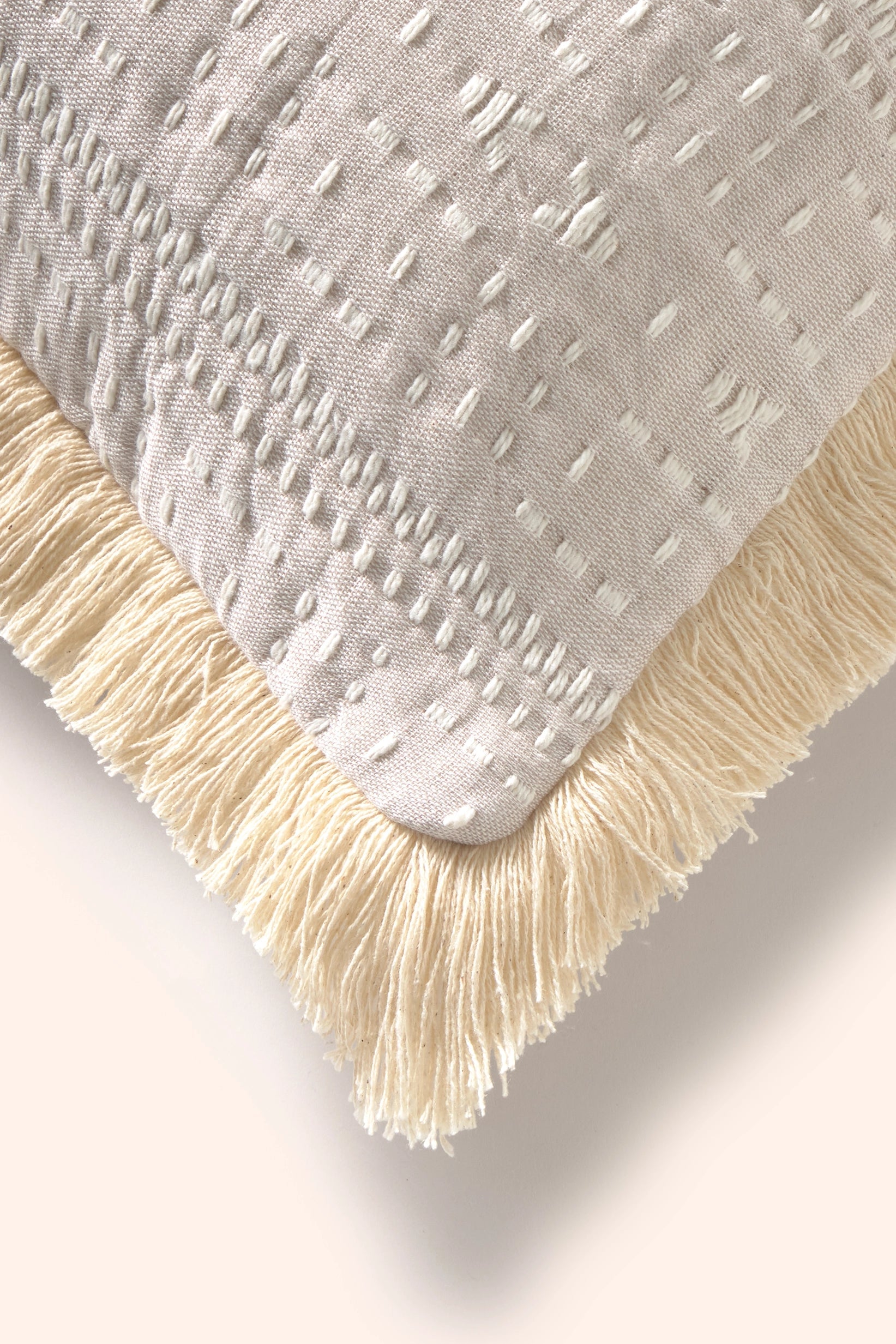 Funda cojín 45x45 de algodón jacquard beige con detalles en crudo y acabado en flecos, detalle de los flecos.