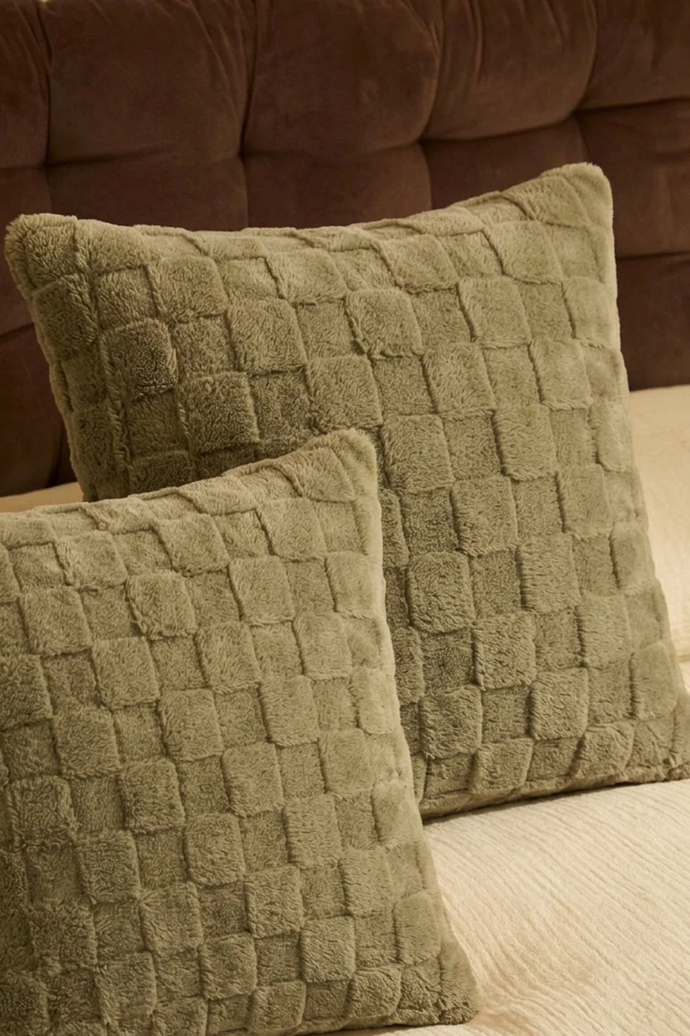 Dos cojines decorativos verdes con relieve damero sobre la cama